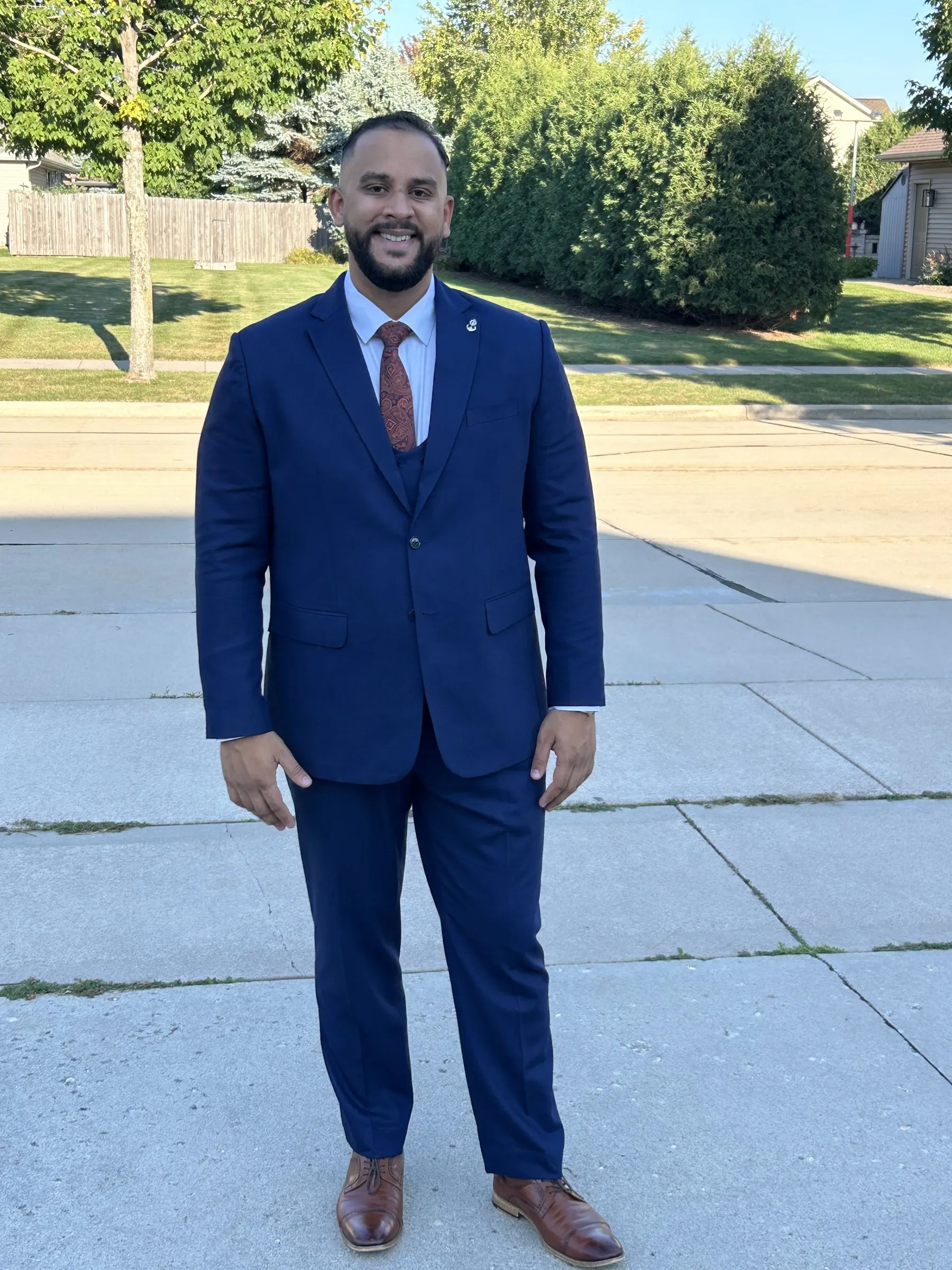 Addy in a navy three-piece suit, smiling at the camera on a sunny street